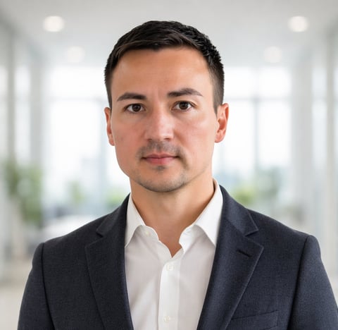 Professional headshot of a man in a dark blazer and white shirt against a blurred office background